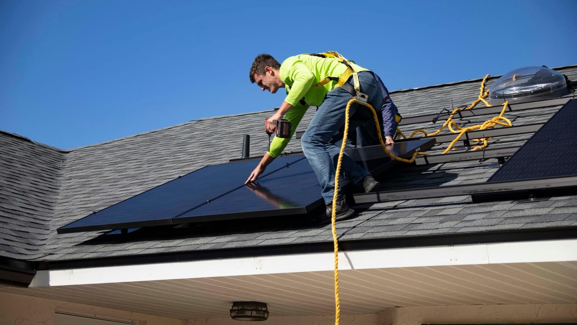 Solar installer fastening a roof attachment with a drill on a shingle roof